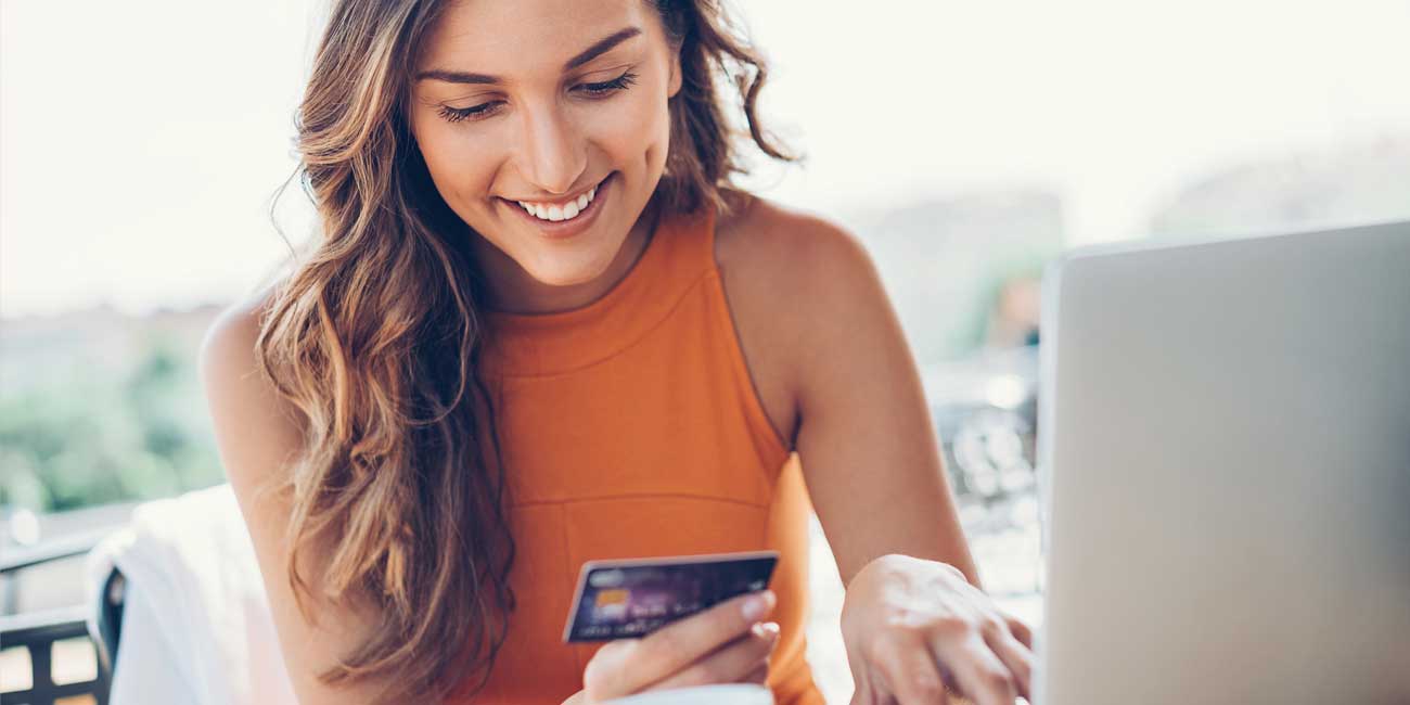 woman in orange shirt holding a credit card in front of a laptop