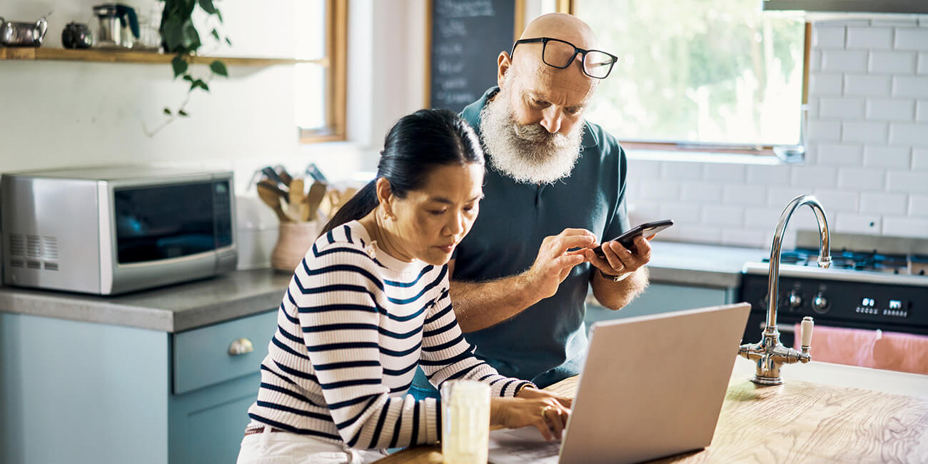 A couple in their kitchen researching home services on a laptop and about to make a call