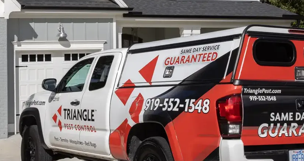 Residential pest control truck from Triangle Pest Control sitting in the driveway of a gray home